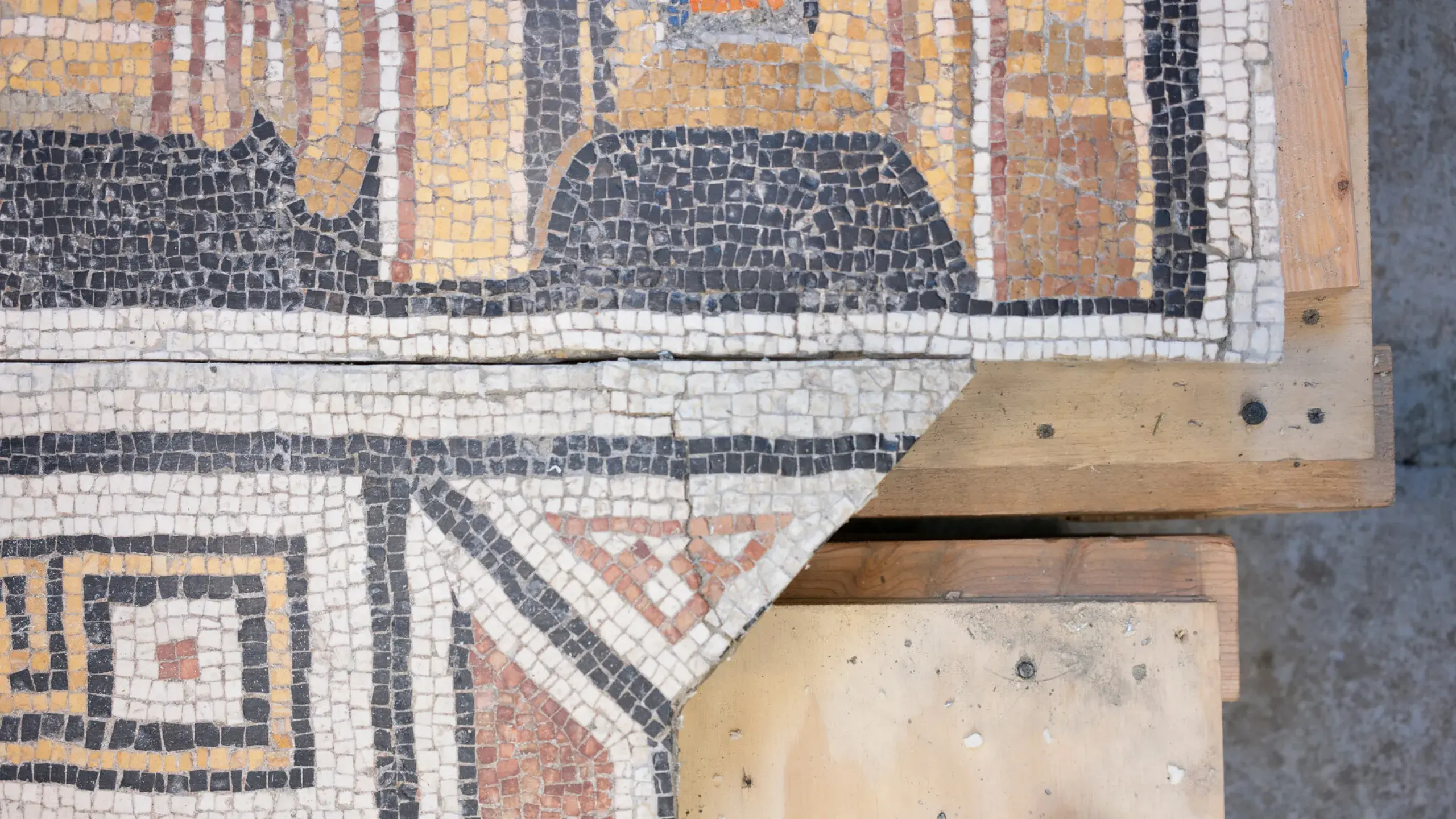 Detail of a mosaic with black, white, and red tesserae in a geometric pattern on a section of plywood.
