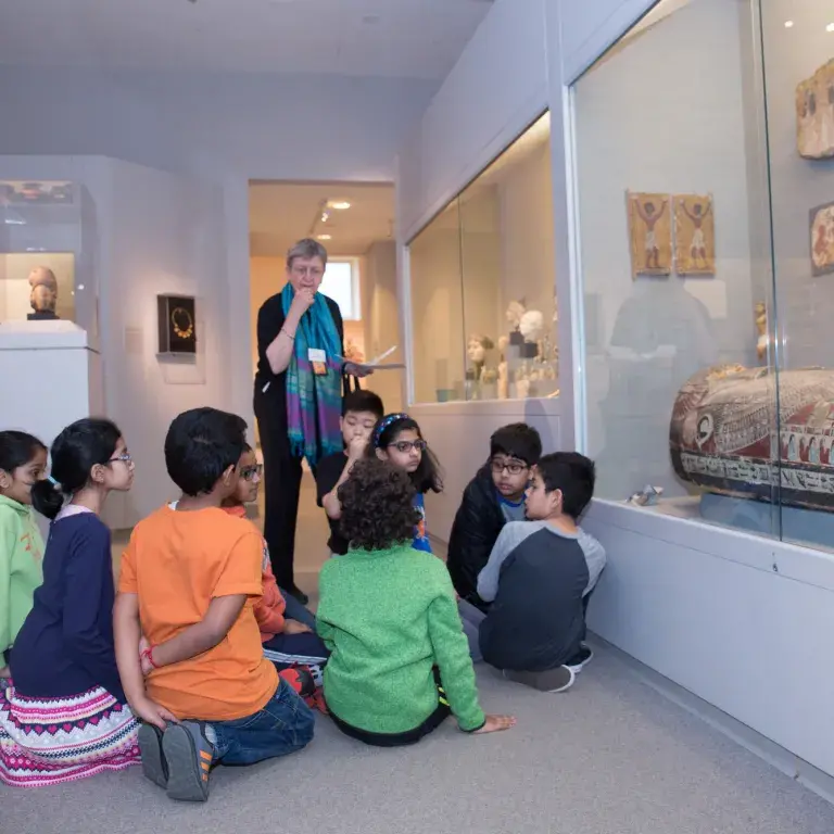 A docent speaks to a group of students about a mummy case.