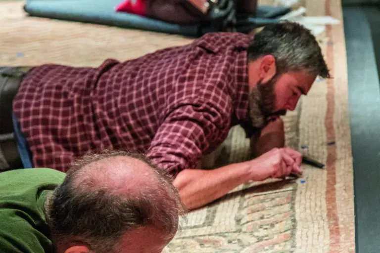 Three people working on the ground, inspecting small pieces of a large mosaic they are installing.