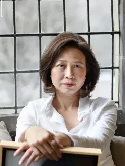 Anne Cheng sitting on a backwards turned chair with her hands crossed in front of a window.